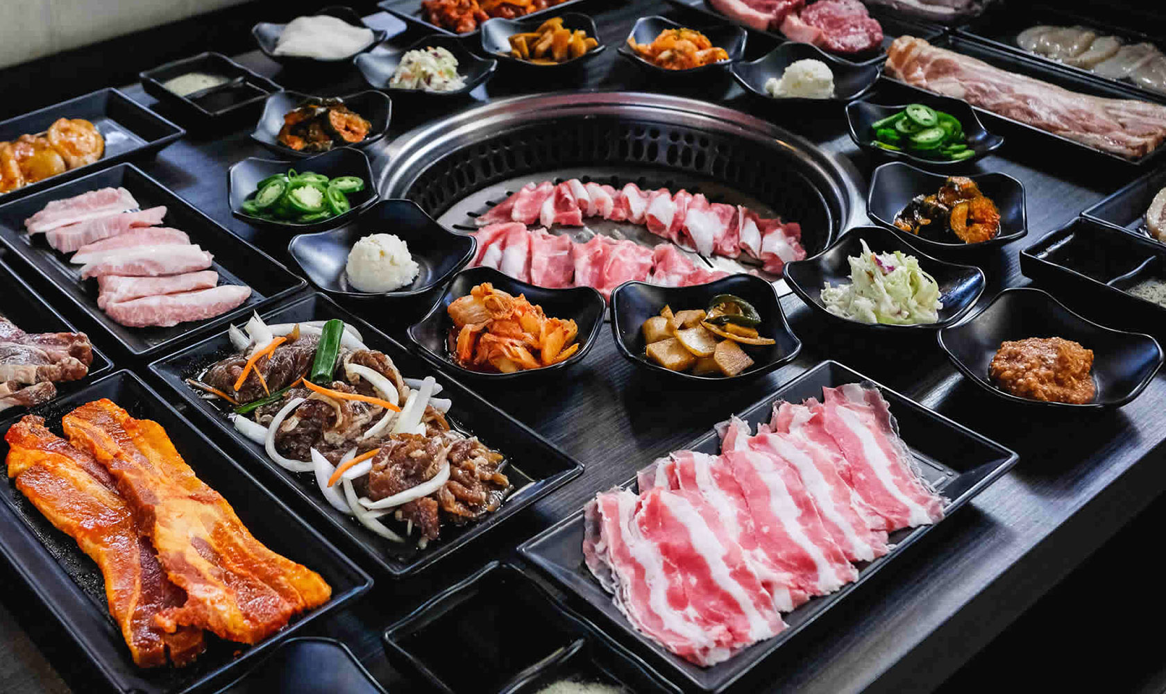 A full Korean BBQ spread at Lanjie — a center grill ringed with marbled raw meats and rows of banchan